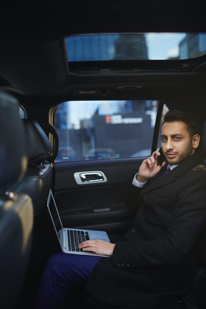 Businessman in a suit working on a laptop while talking on the phone in the backseat of a car