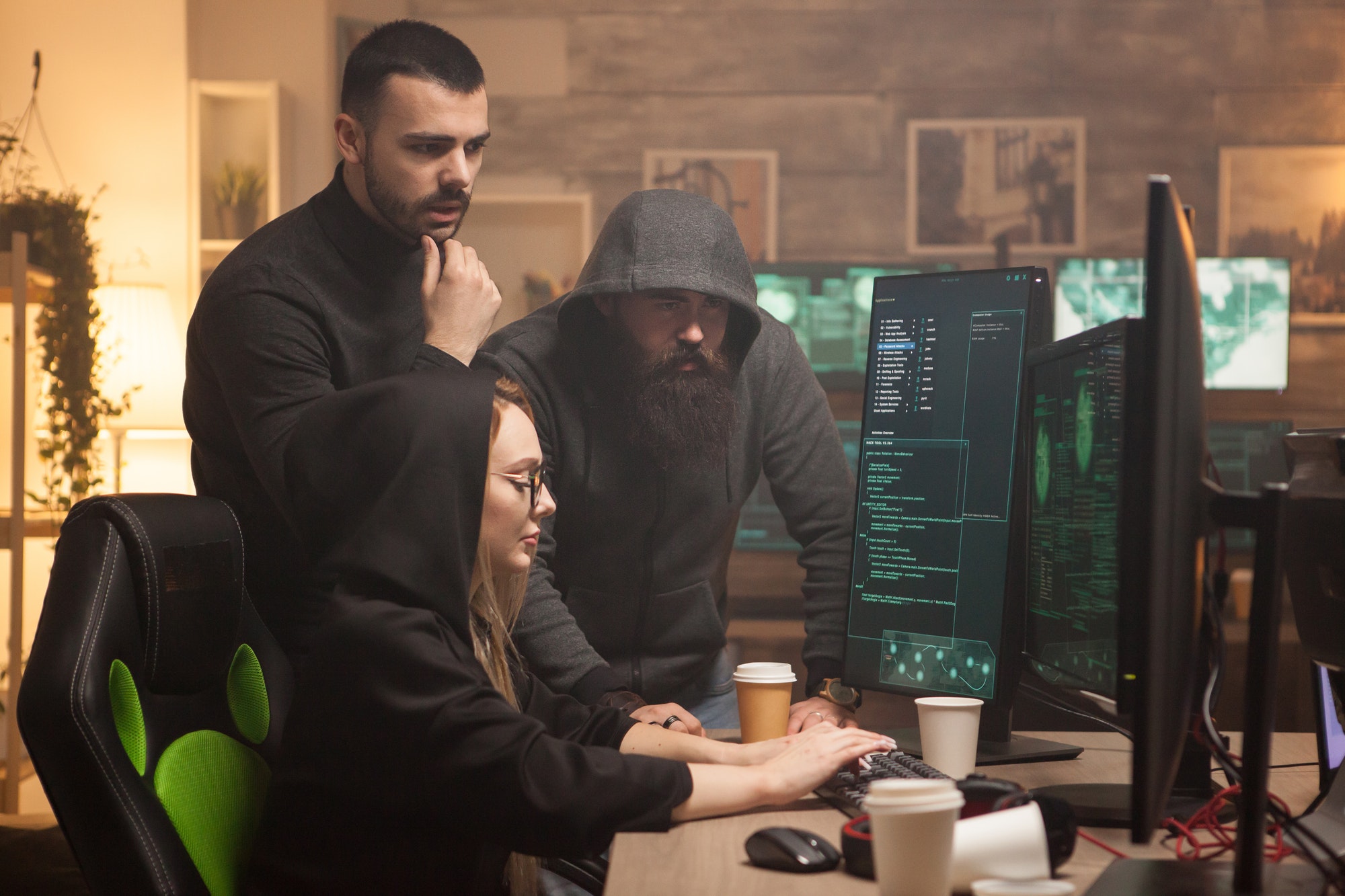 Three cybersecurity professionals intently analyze code on computer monitors in a cozy office setting OMEX Cyber Security