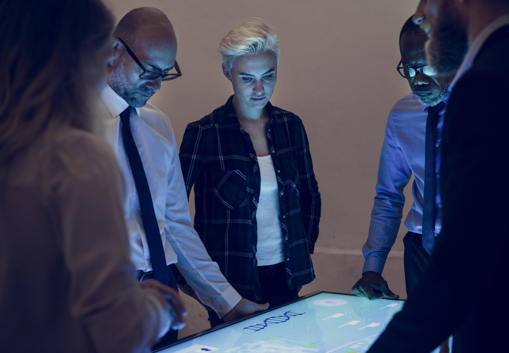 A diverse group of professionals engaged around an interactive table display, analyzing data in a collaborative work environment