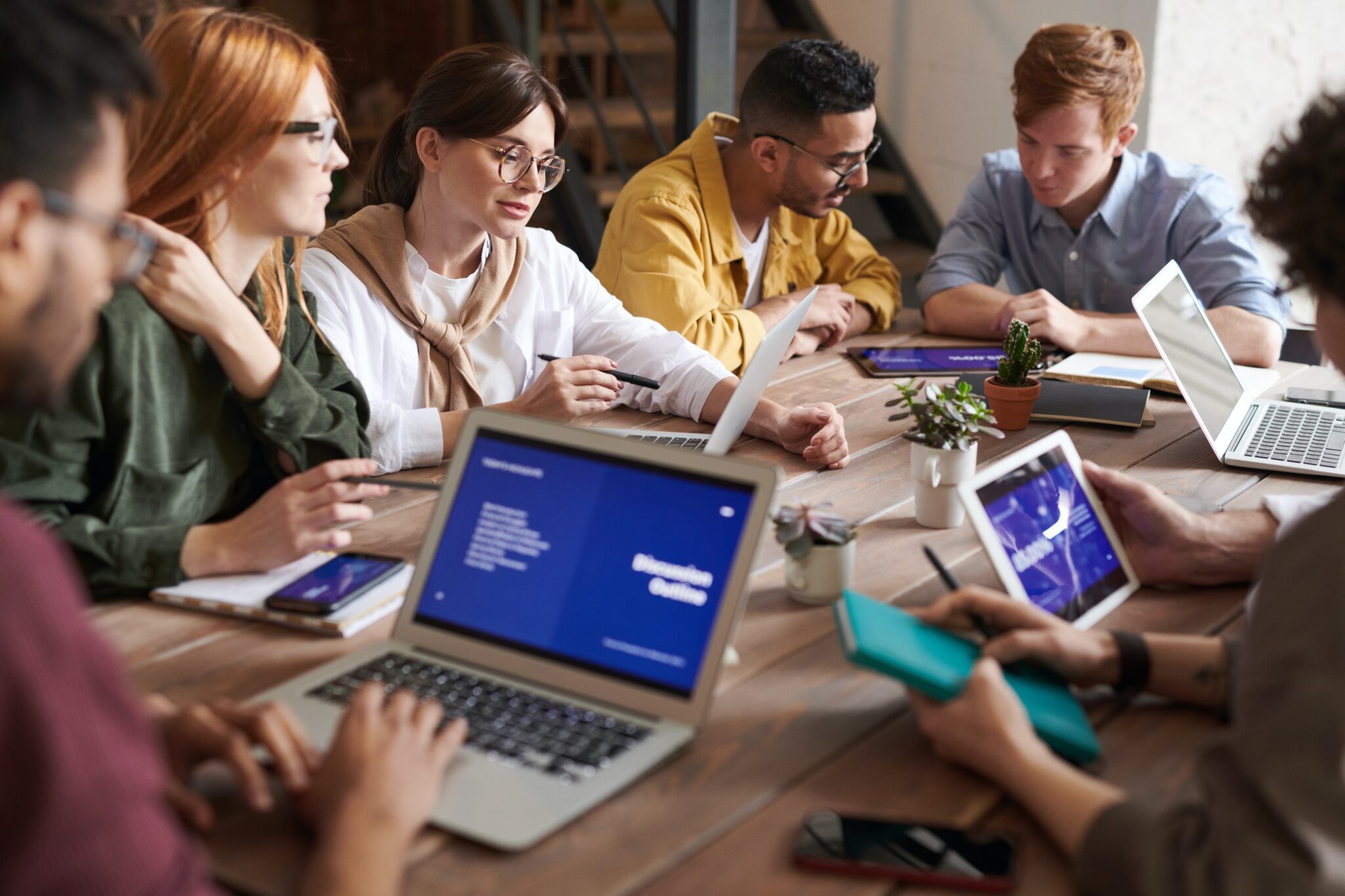 Diverse team of professionals engaged in a collaborative meeting with laptops and digital tablets around a wooden table