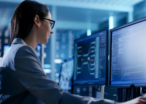 Female cybersecurity professional analyzing data on multiple computer monitors in a network operations center